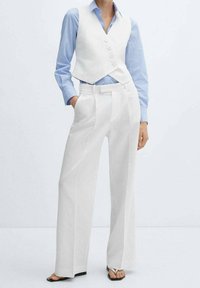 Gilet bianco su misura con bottoni, abbinato a pantaloni bianchi a vita alta. Camicia a maniche lunghe a righe Blu chiaro. Tessuto morbido e gambe larghe.