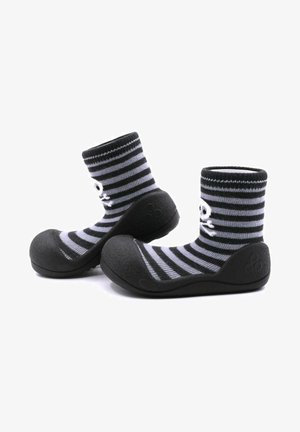 Calcetines a rayas en negro y gris con suela de goma. La parte superior es de tela de punto, y la puntera presenta un acabado redondeado y texturizado.