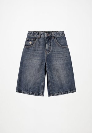 Ντένιμ σορτς σε σκούρο μπλε, με χαλαρή εφαρμογή, σχέδιο πέντε τσεπών, ορατές ραφές και σύμβολο ειρήνης στην μπροστινή τσέπη.