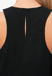 Μαύρο άνετο τοπ χωρίς μανίκια με άνοιγμα στον αυχένα, κατασκευασμένο από υφή που προσφέρει μια απαλή αίσθηση.