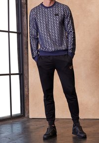 Sudadera navy con patrón de logo blanco, mangas largas y puños de canalé, combinada con joggers negros y zapatillas deportivas negras.