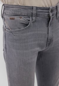 Gray denim jeans with a slim fit, featuring front pockets, a small logo tag, and subtle texture. Classic design with minimal accents.