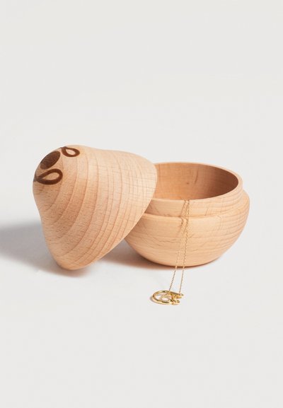 Round wooden container with removable lid next to it, holding a delicate gold necklace with circular pendants spilling out.