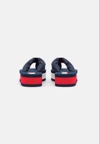 Navy blue flip-flops with padded straps, featuring a red and white layered platform, and a textured black sole. Logo on top.