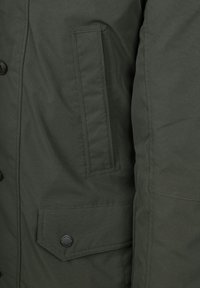 Olijfgroene geïsoleerde jas met een gladde textuur, voorzien van een zijzak met klep en een knoopsluiting aan de voorkant.