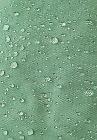 Wasserabweisender Stoff in sanftem Grün mit einer strukturierten Oberfläche, auf der deutlich sichtbare Wassertropfen verteilt sind.