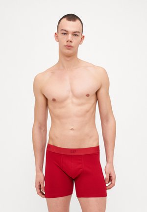 Boxers rojos de algodón con un ajuste ceñido y una cinturilla con logo. La tela parece suave con detalles de costura mínimos.