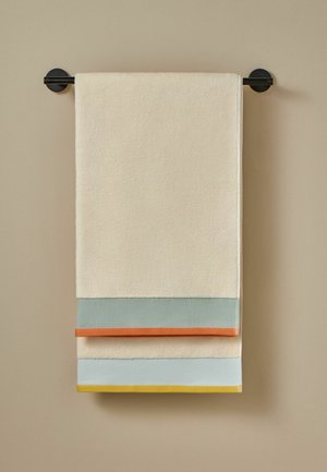 Toalla beige con rayas horizontales en azul claro, naranja y amarillo, colgada ordenadamente en una barra de toallas negra contra una pared beige.