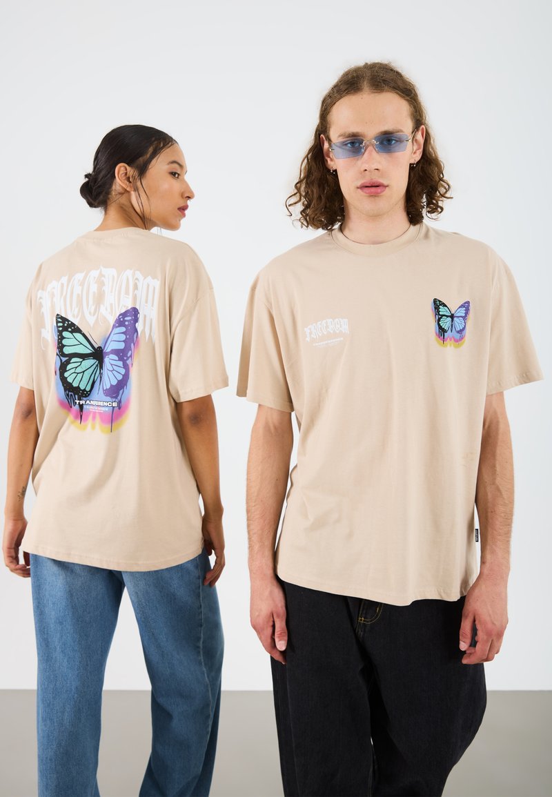 Beige oversized t-skjorte laget av bomull, med et stort sommerfuglgrafikk på baksiden og en mindre sommerfugl på venstre front.