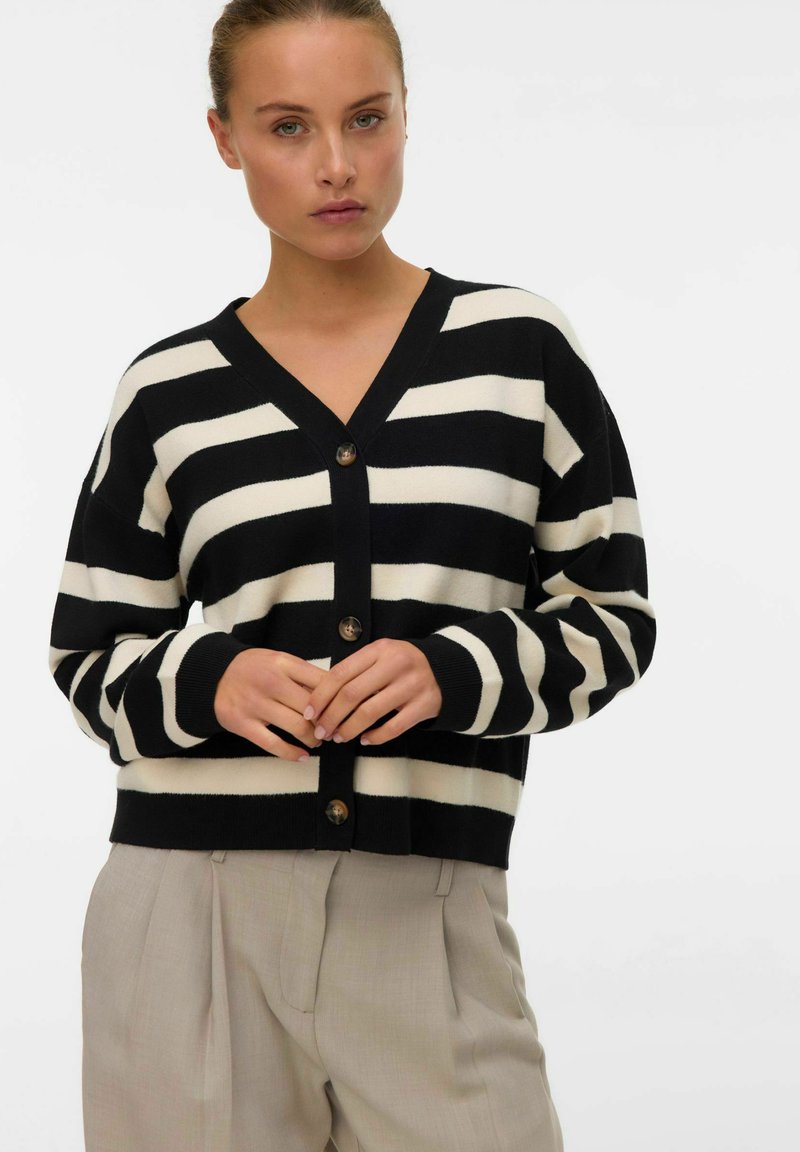 Zwart en crèmekleurige gestreepte cardigan met een V-hals, knoopsluiting en lange mouwen. Draagt over lichtgekleurde broeken. Zachte, gebreide textuur.