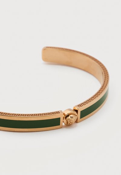 Χρυσό βραχιόλι μανσέτα με σκούρο πράσινο σμάλτο και άκρες με μοτίβο ελληνικού κλειδιού σε λευκό φόντο.