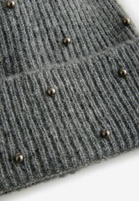 Bonnet en tricot gris avec un motif en côtes texturé, comportant de petites clous métalliques incrustés pour un détail supplémentaire.
