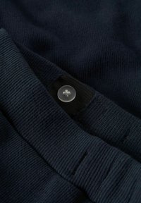 Mørkeblått strikket stoff med knappdetalj. Stoffet har en tekstur med kjerner, og knappen er klar med et dekorativt design.