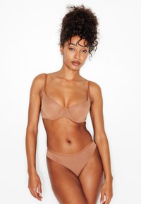 Reggiseno marrone chiaro e slip bikini abbinati realizzati in tessuto liscio. Il reggiseno presenta ferretto e spalline regolabili; design complessivamente senza cuciture.
