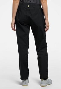 Svarta, lätta byxor med elastisk midja, smalnande design och dragkedjeöppningar vid benen, i kombination med grå skor med gula accenter.