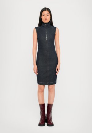 Vestido de mezclilla sin mangas con cuello alto, cremallera frontal, color azul oscuro y costuras en contraste. Combinado con botas de tobillo burdeos brillantes.