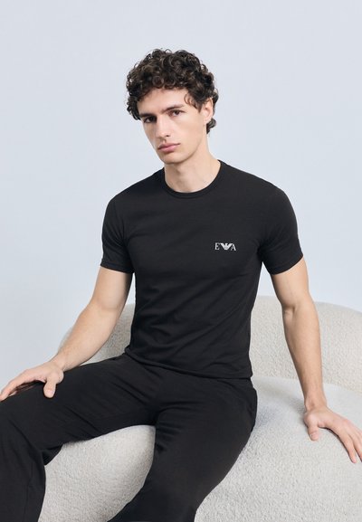 Melnā kokvilnas t-krekls ar nelielu baltu logo uz krūtīm. Audums izskatās mīksts, ar klasisku apaļu apkakli un īsām piedurknēm.