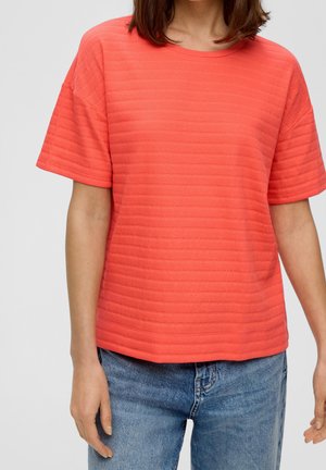 Korallinvärinen, lyhythihainen t-paita, jossa on ribbineulos ja pyöreä pääntie, yhdistetty vaaleansinisiin farkkuihin.