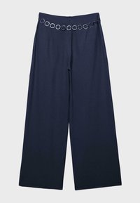 Pantalon large bleu marine avec ceinture chaîne décorative à anneaux argentés à la taille, fermeture éclair frontale et texture de tissu lisse.