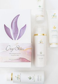 Hautpflegeprodukt-Set mit einer weißen Box mit violettem Blumenmuster, einer Reinigungsmilch, einem Toner und einer Creme in weißen Tube, alle mit goldenen Akzenten.
