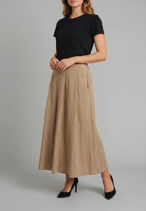 Donna che indossa un top nero a maniche corte, gonna beige a vita alta, lunghezza alla caviglia, con tasche, e décolleté nere con punta.