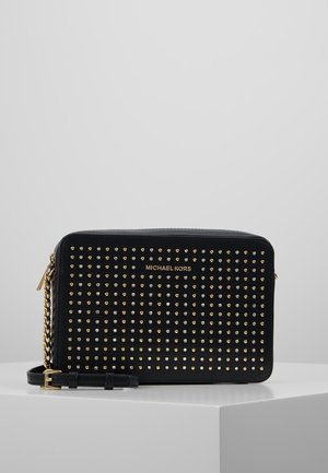 Czarna torebka Michael Kors na ramię z złotymi i srebrnymi ćwiekami, złotym łańcuszkiem i zamkiem błyskawicznym, leżąca na białej powierzchni.