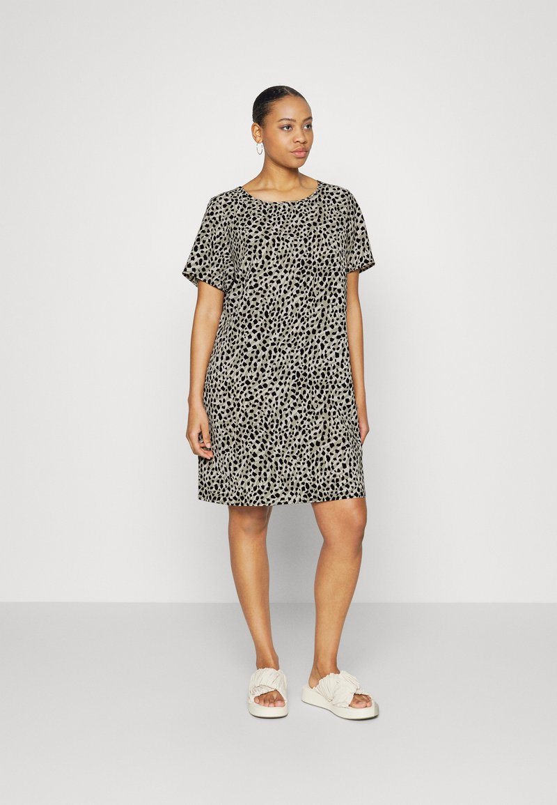Robe imprimée léopard beige et noire, à manches courtes, coupe décontractée, longueur genoux. Portée avec des chaussures blanches à enfiler, texture lisse.