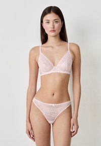Lichtroze kant bralette en string set met gegolfde randen, bloemmotieven en delicate bandjes, met een kleine strikaccent op de string.