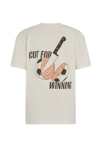 Valkoinen t-paita, jossa on graafinen kuva veitsestä viiltämässä jalkapalloa, joka näyttää salamimakkaralta, ja tekstissä "VOITTOPERUSTE" takana.