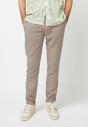 Beige Baumwollhosen mit schlanker Passform, mit umschlagenen Knöcheln und Seitentaschen, kombiniert mit beige-creamfarbenen Sneakers.