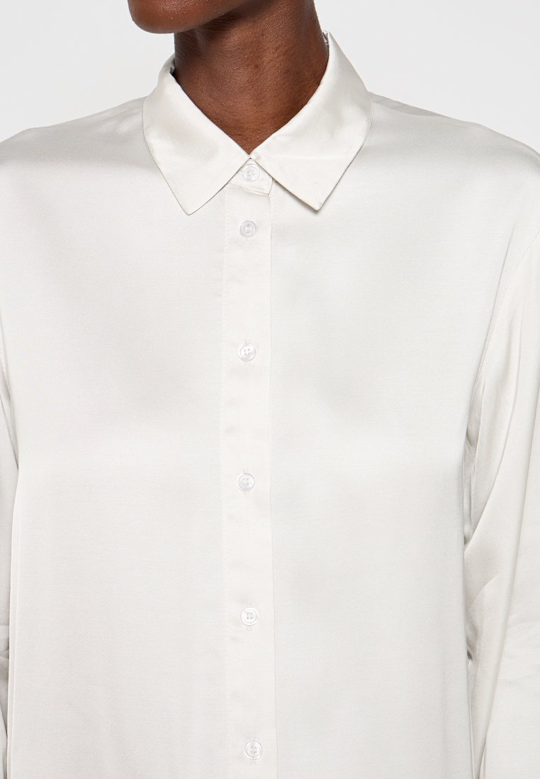 Weiße Satinbluse mit spitzem Kragen, Knopfleiste auf der Vorderseite und glatter Textur. Hat lange Ärmel und eine klassische Passform.