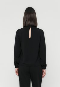 Black long-sleeve shirt with a textured fabric, featuring a keyhole cutout at the back and button cuffs. Simple design without patterns.