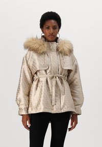 Bež satenasta pufasta jakna s kapuco iz umetnega krzna, pasom, velikimi sprednjimi žepi, jezikastim teksturo in prevelikimi rokavi.