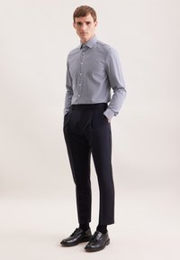 Niebieska i biała koszula w kratę z kołnierzykiem, połączona z ciemnymi dopasowanymi spodniami i czarnymi butami. Gładka tkanina i dopasowany krój.