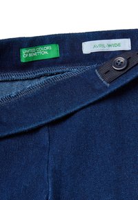 Tmavě modré džíny s širokými nohavicemi. Štítky uvádějí "United Colors of Benetton" a "Avril-Wide." Mají zapínání na knoflík a zip.