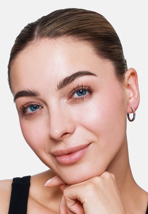 Boucle d'oreille en argent avec un petit accent de pierre précieuse colorée. Texture lisse et finition polie, portée par une personne à la peau claire et aux cheveux foncés.