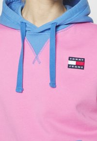 Felpa con cappuccio con corpo rosa e cappuccio blu. Presenta un piccolo etichetta "TOMMY JEANS" in nero, rosso e bianco sul davanti.
