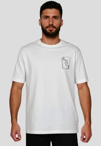 Camiseta de algodón blanca con mangas cortas, que presenta un pequeño gráfico negro de un personaje en la zona izquierda del pecho. Diseño clásico de cuello redondo.