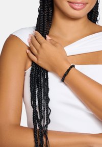 Black beaded bracelet featuring smooth round and textured beads, worn on a wrist, against a light background with white clothing.