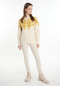Pulover crem cu un model de frunze galbene, asortat cu pantaloni ajustați bej și cizme bej cu șireturi. Textură moale, fit relaxat și guler tip crew.