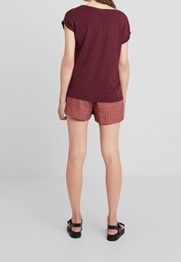 Burgundy kortärmad topp tillsammans med mönstrade röda shorts. Skorna är svarta sandaler. Slätt tyg och avslappnad passform.