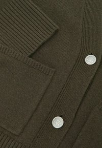 Tamno zelena pletena vestica s rebrastom teksturom, prednjim džepom i srebrnim gumbima s logotipom.