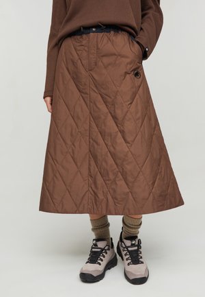 Gonna midi trapuntata marrone indossata con calzini beige e scarpe da trekking grigie, abbinata a una maglia marrone a maniche lunghe.