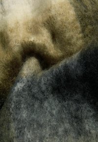 Tekstūra auduma zaļos, brūnos un melnos toņos ar mīkstu, pūkainu izskatu, kurā ietilpst dažādu krāsu un biezuma sajaukums.