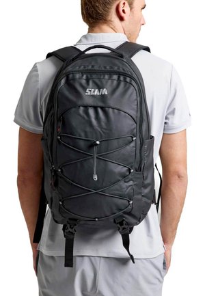 Un hombre con una camisa blanca lleva una mochila negra SLAM con bolsillos con cremallera y cordón elástico sobre un fondo blanco.