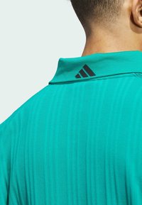 Tyrkysové polo tričko s texturovaným vzorem, které má černý detail loga s třemi pruhy na límci a klasický design límce.