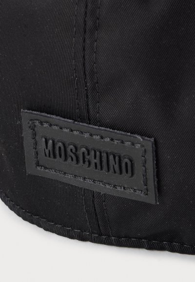 Gros plan sur un tissu noir avec une étiquette rectangulaire cousue montrant un texte en relief "MOSCHINO".