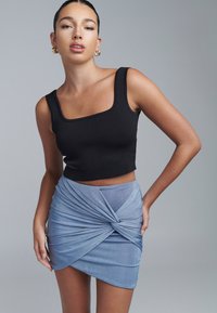 Černý žebrovaný crop top se čtvercovým výstřihem, kombinovaný se světle modrou mini sukní s drapírovaným detailem a uzlem. Hladká textura.