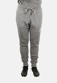 Graue Sweatpants mit elastischem Bund und Kordelzug, mit schmalem Schnitt und gerippten Bündchen, getragen zu schwarzen Fußballschuhen.