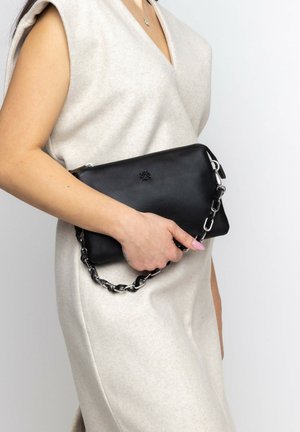 Clutch in pelle nera con finitura texture, dotata di una tracolla in catena argentata. È appoggiata su un indumento di un beige chiaro.